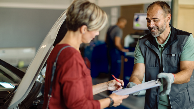 Vehicle technician handing a clipboard to a customer for her to sign a document.